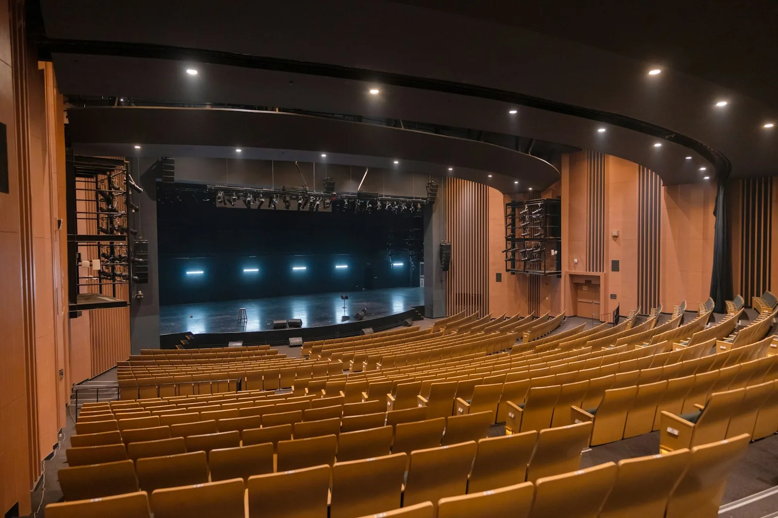 Wide-angle view of an empty modern theatre auditorium with wooden seats and a lit stage, representing the theatrical productions inspired by Viv Nicholson's story including the Olivier Award-winning West End musical Spend Spend Spend